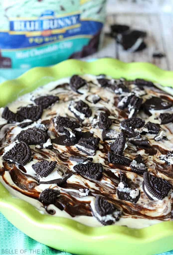 A chocolate ice cream cake in a green pie plate topped with fudge and Oreos 