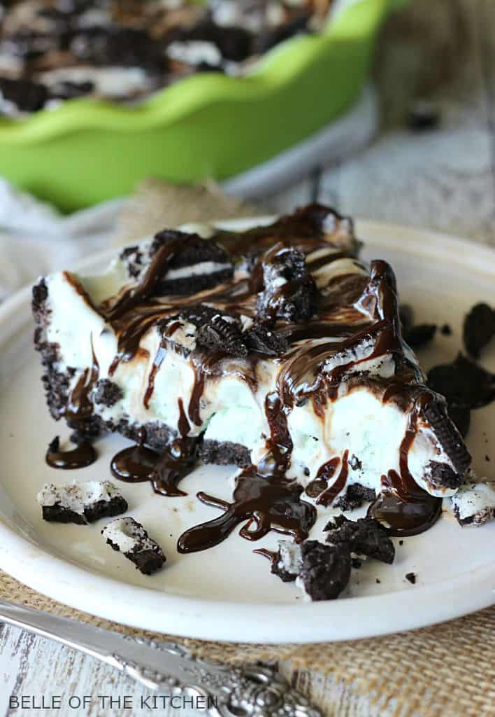 A piece of chocolate ice cream cake on a plate, with Chocolate fudge and Oreos 