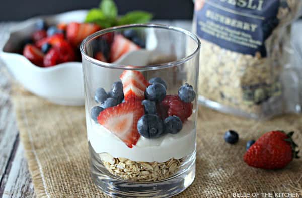 A glass filled with layers of cheesecake, fruit, and granola