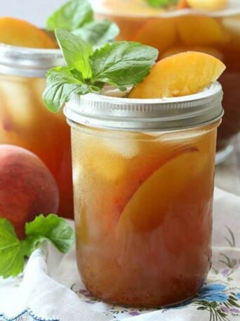 A close up of a glass of peach tea filled with mint and peach slices