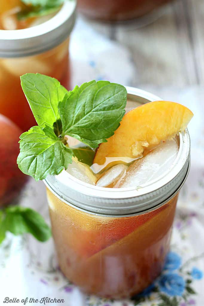 A close up of a glass of peach tea filled with mint and peach slices