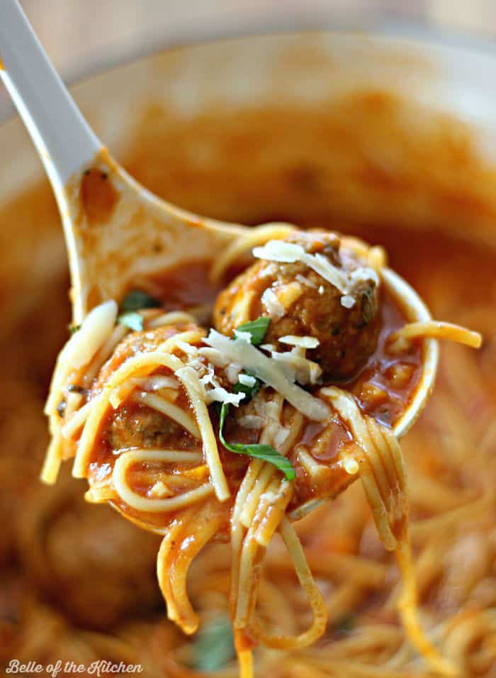 A close up of a spoon holding spaghetti and meatballs topped with cheese and basil