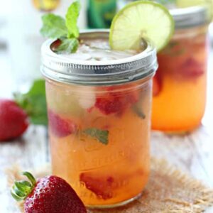 A close up of mason jars filled with strawberry mojitos, fresh strawberries, mint, and lime slices on the rim