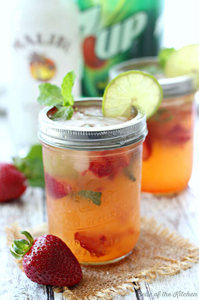 A close up of mason jars filled with strawberry mojitos, fresh strawberries, mint, and lime slices on the rim