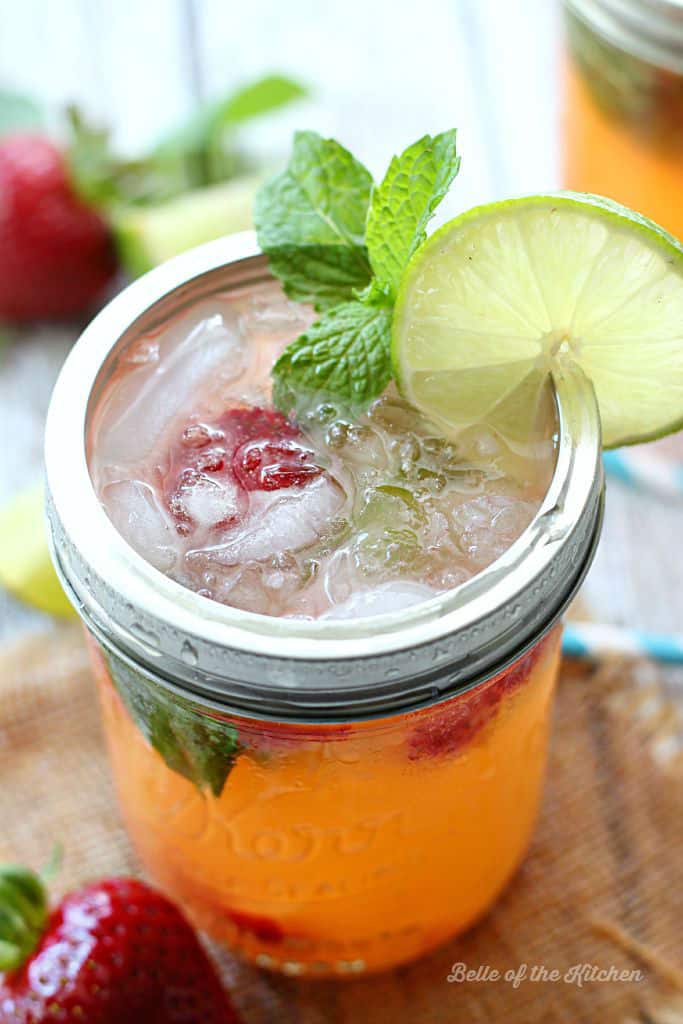 A close up of mason jars filled with strawberry mojitos, fresh strawberries, mint, and lime slices on the rim