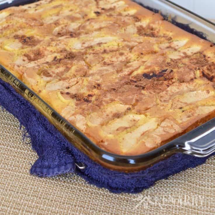 a baking dish filled with baked apple cake wrapped in a blue towel