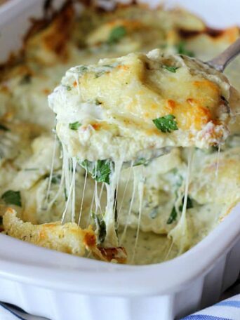 a close up of a spoon pulling out cheesy ravioli topped with parsley