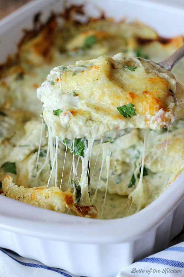 a close up of a spoon pulling out cheesy ravioli topped with parsley