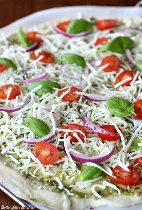 a pizza topped with red onions, tomatoes, and basil ready to be baked