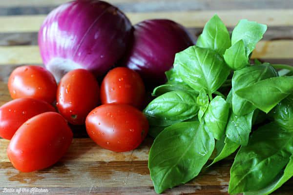 A cutting board is filled with red onion, tomatoes, and basil leaves