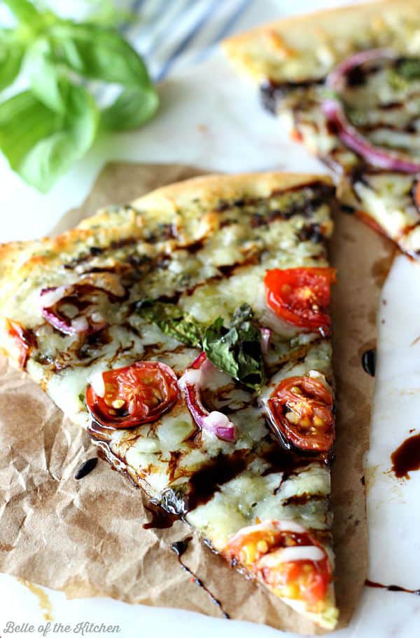 a slice of pizza topped with red onions, tomatoes, and basil and drizzled with balsamic