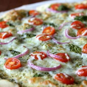 a pizza topped with red onions, tomatoes, and basil
