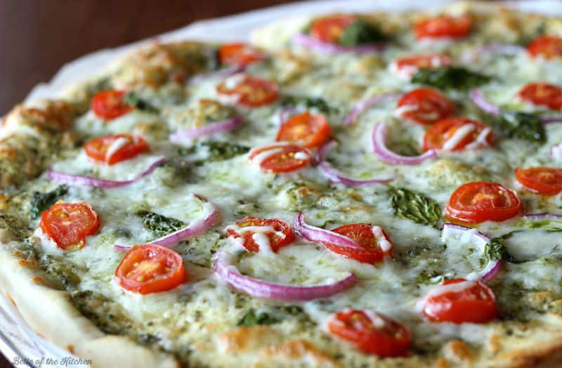 a pizza topped with red onions, tomatoes, and basil