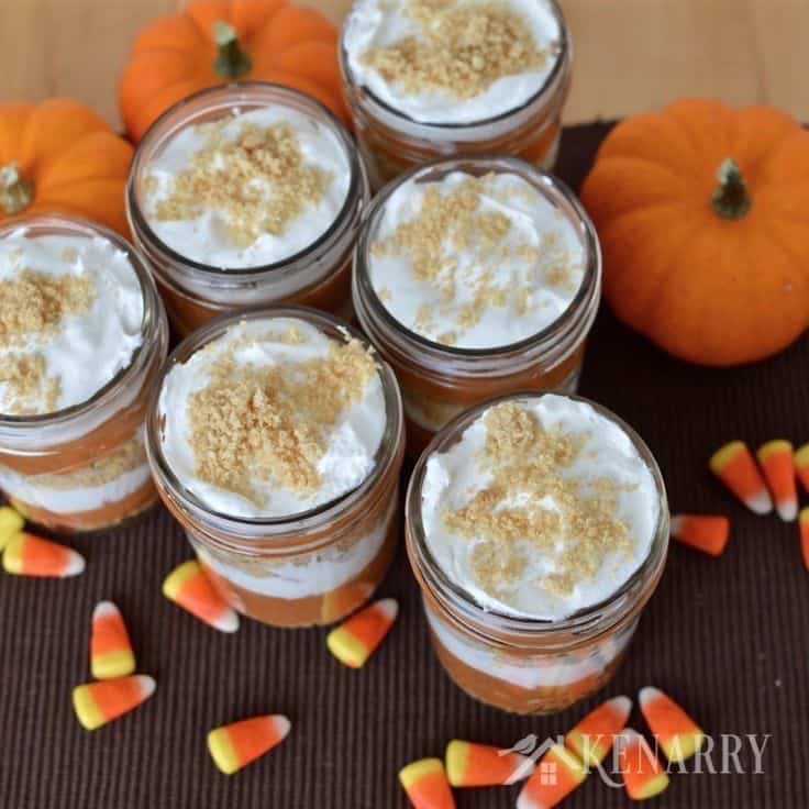 jars with layers of pumpkin, cream cheese, and graham cracker crumbs with mini pumpkins in the background