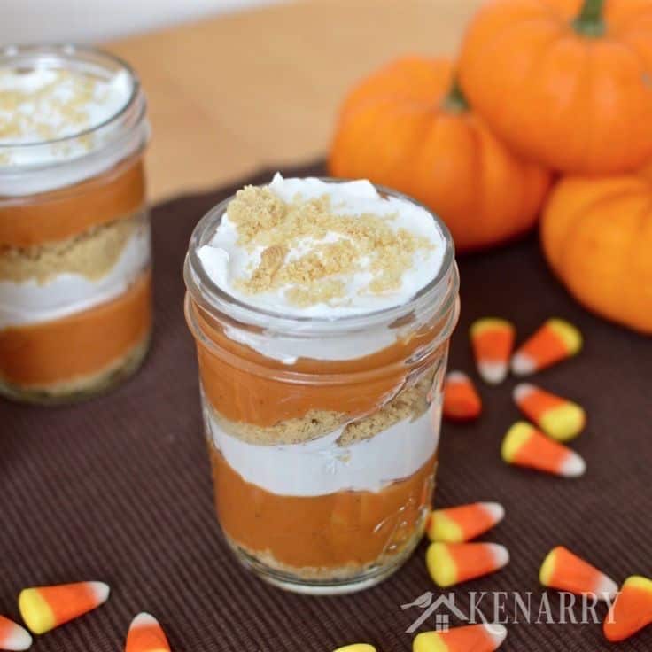jars with layers of pumpkin, cream cheese, and graham cracker crumbs with mini pumpkins in the background