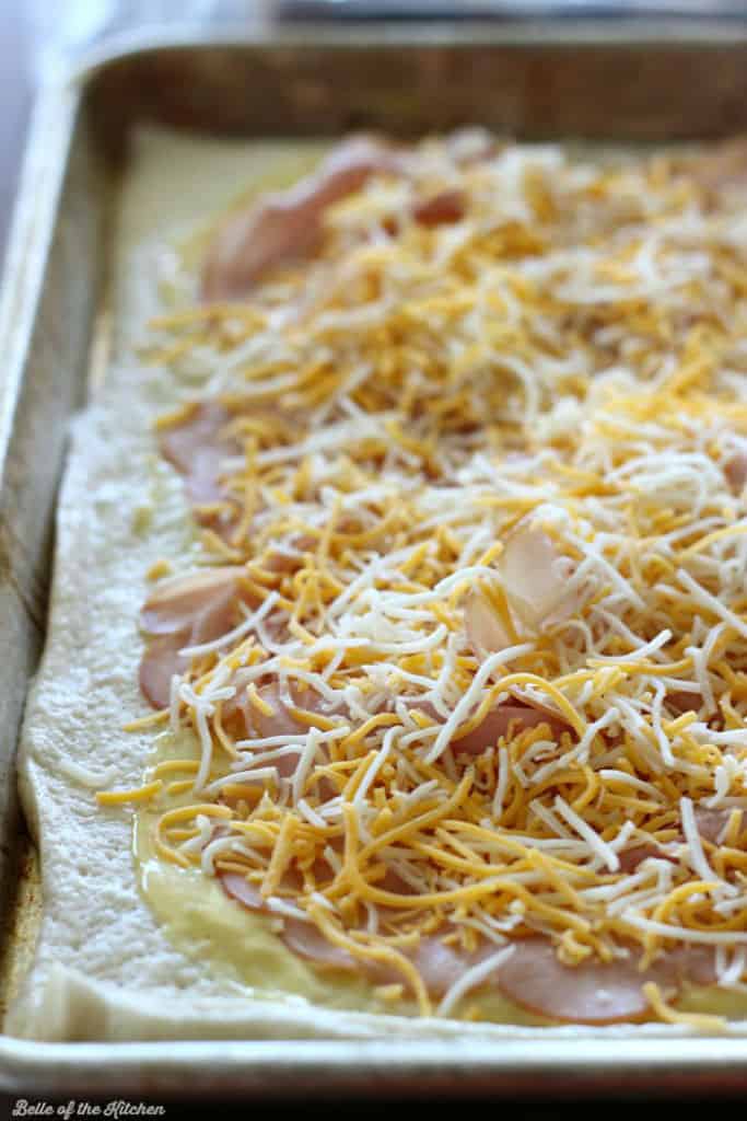 pizza dough on a sheet pan topped with ham and cheese