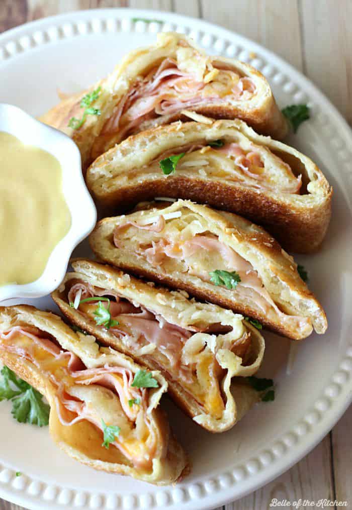 A plate of ham and cheese Stromboli with a bowl of honey mustard