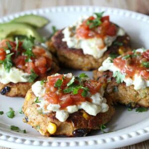 A plate full of tuna cakes topped with salsa, cilantro, and avocado