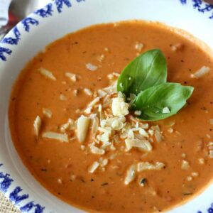 A bowl of tomato soup topped with shredded cheese and basil