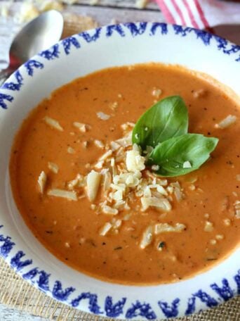 A bowl of tomato soup topped with shredded cheese and basil