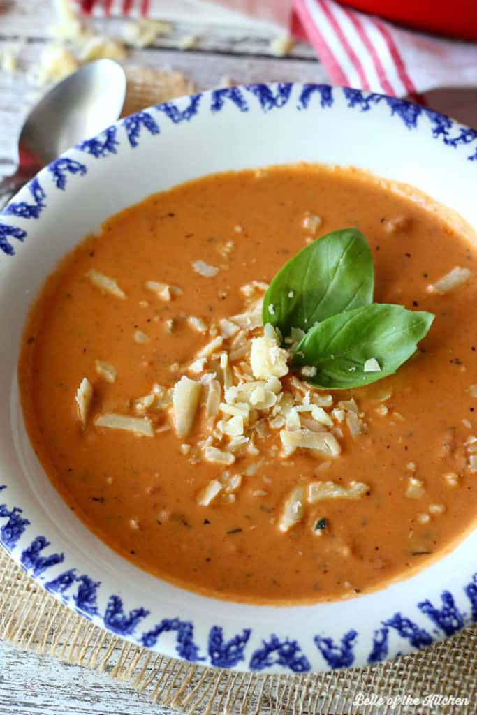 A bowl of tomato soup topped with shredded cheese and basil