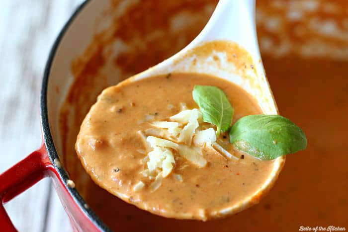 A close up of a spoon filled with tomato soup topped with shredded cheese and basil