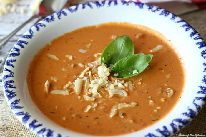 A bowl of tomato soup topped with shredded cheese and basil