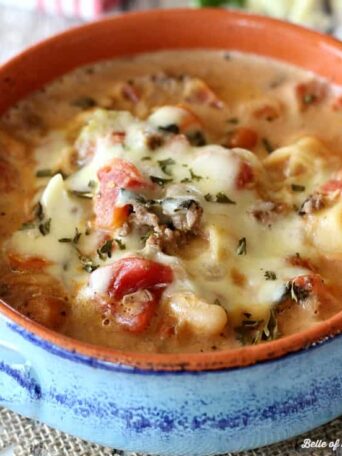 A bowl of tortellini soup with melted cheese on top