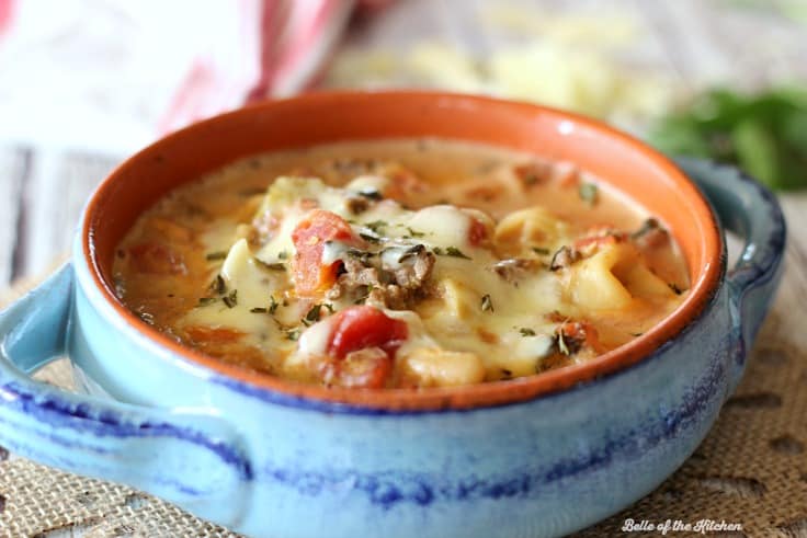 A bowl of tortellini soup with melted cheese on top