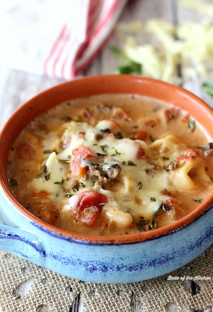 A bowl of tortellini soup with melted cheese on top