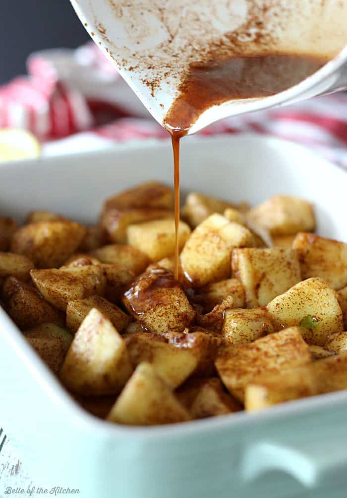 baked apples in a dish with sauce being poured over