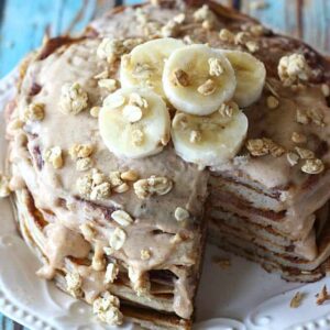 A stack of pancakes with a bite taken out, covered in syrup, granola and bananas