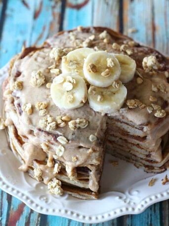 A stack of pancakes with a bite taken out, covered in syrup, granola and bananas