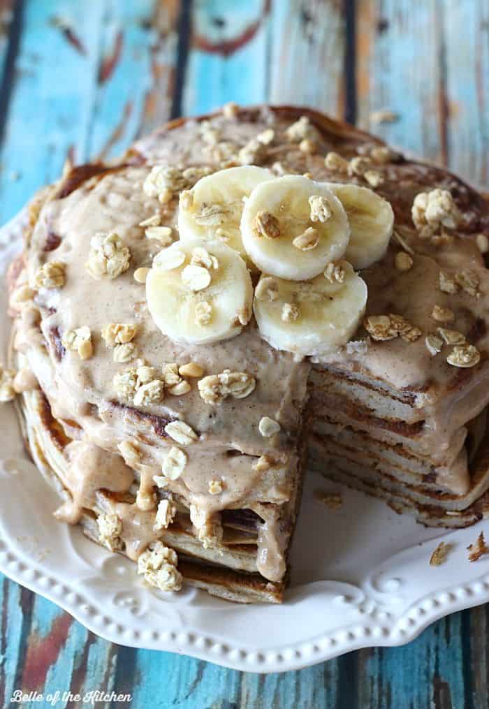 A stack of pancakes with a bite taken out, covered in syrup, granola and bananas