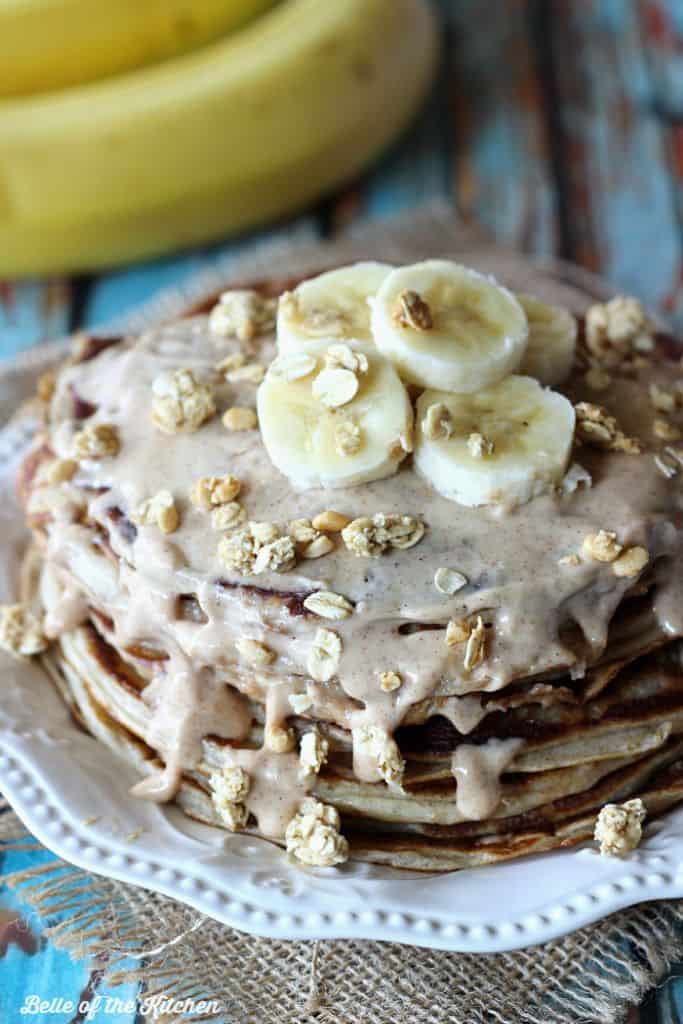 A stack of pancakes covered in syrup, granola and bananas