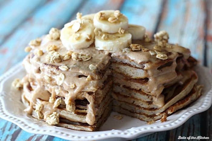 A stack of pancakes with a bite taken out, covered in syrup, granola and bananas