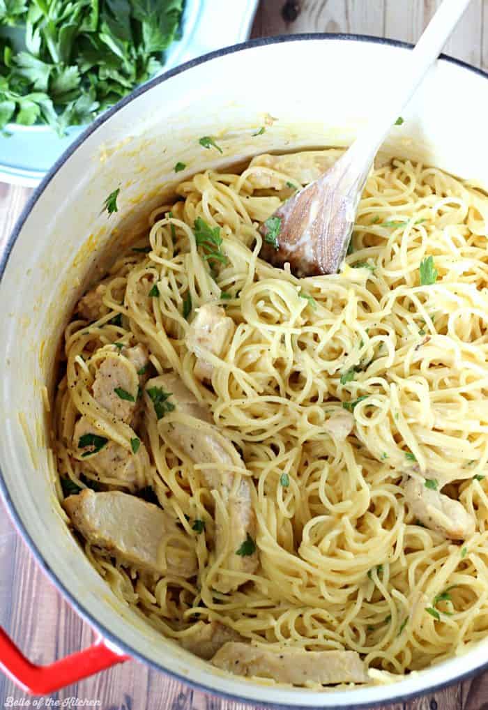 A pot filled with pasta and chicken topped with parsley