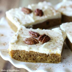 A close up of a sliced pumpkin bar with frosting and pecans on top