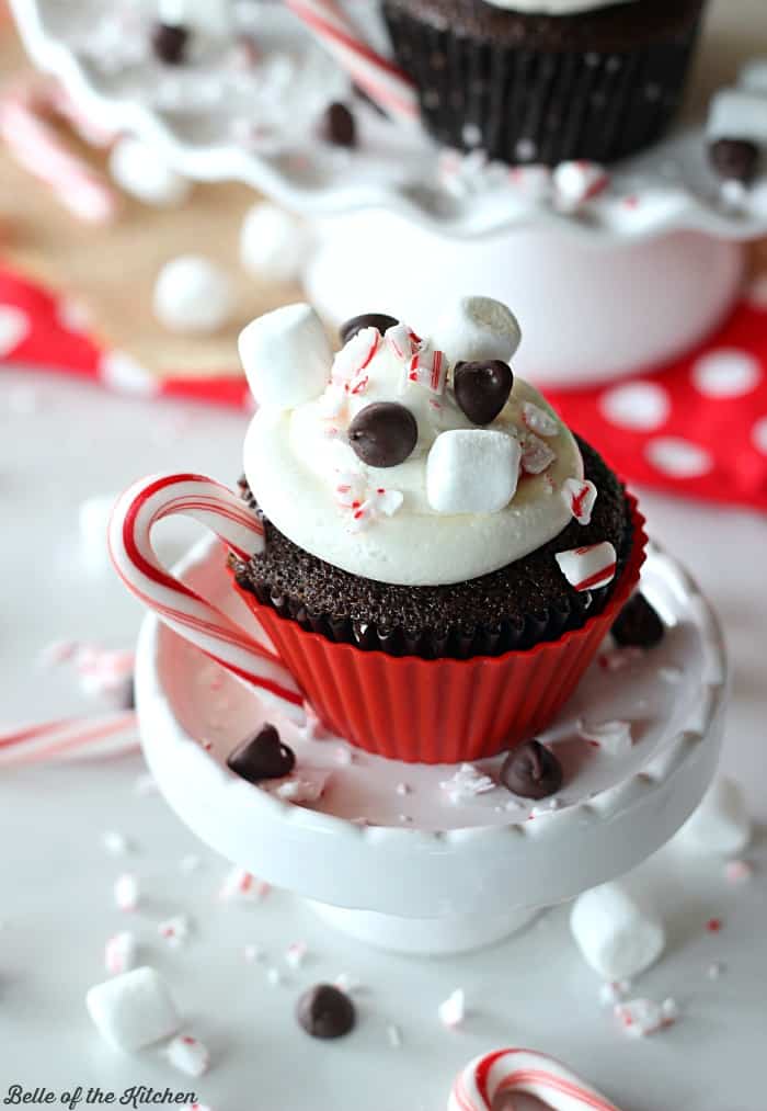 a cupcake with marshmallow frosting, chocolate chips, and a peppermint candy cane handle