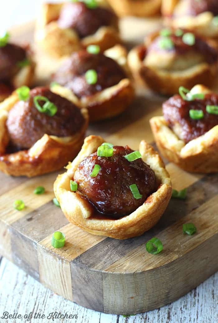 A close up of meatballs in pastry cups on a wooden cutting board