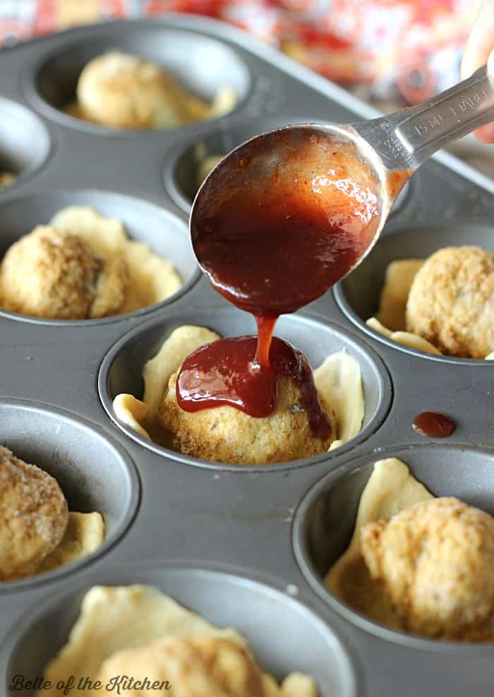 A muffin tin filled with meatballs with sauce being poured on top