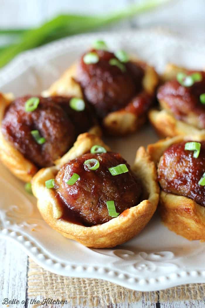 A close up of meatballs in pastry cups on a wooden cutting board