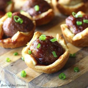 A close up of meatballs in pastry cups on a wooden cutting board