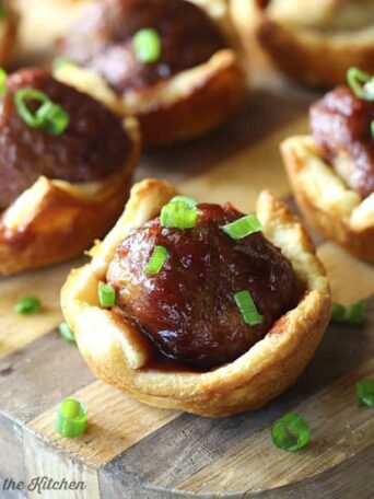 A close up of meatballs in pastry cups on a wooden cutting board