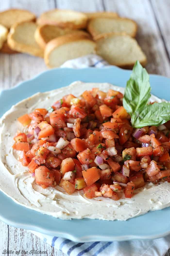 A plate of cream cheese topped with bruschetta and basil