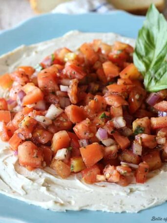 A plate of cream cheese topped with bruschetta and basil