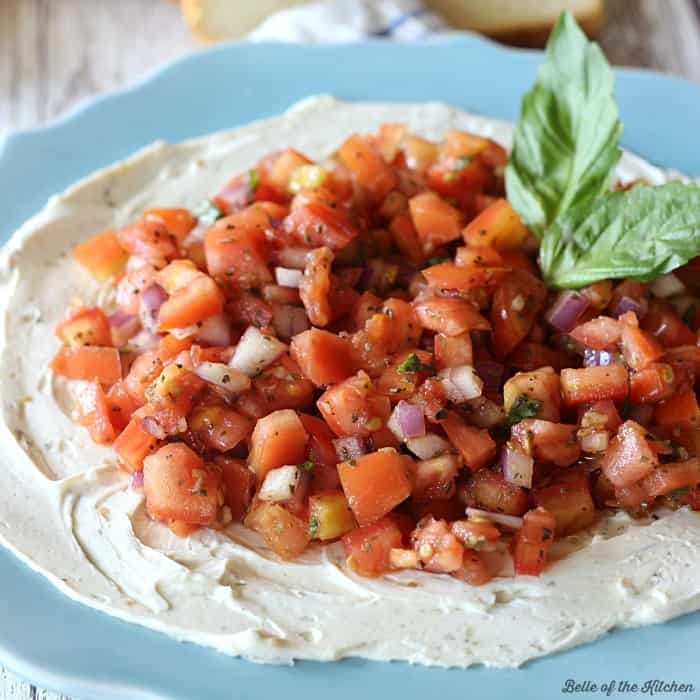 A plate of cream cheese topped with bruschetta and basil