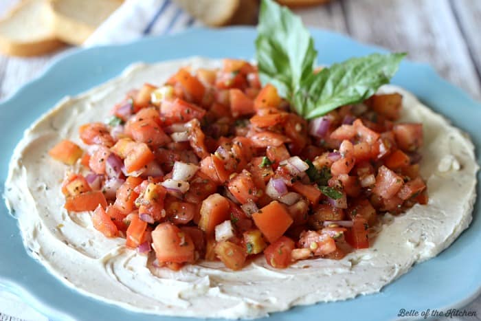 A plate of cream cheese topped with bruschetta and basil