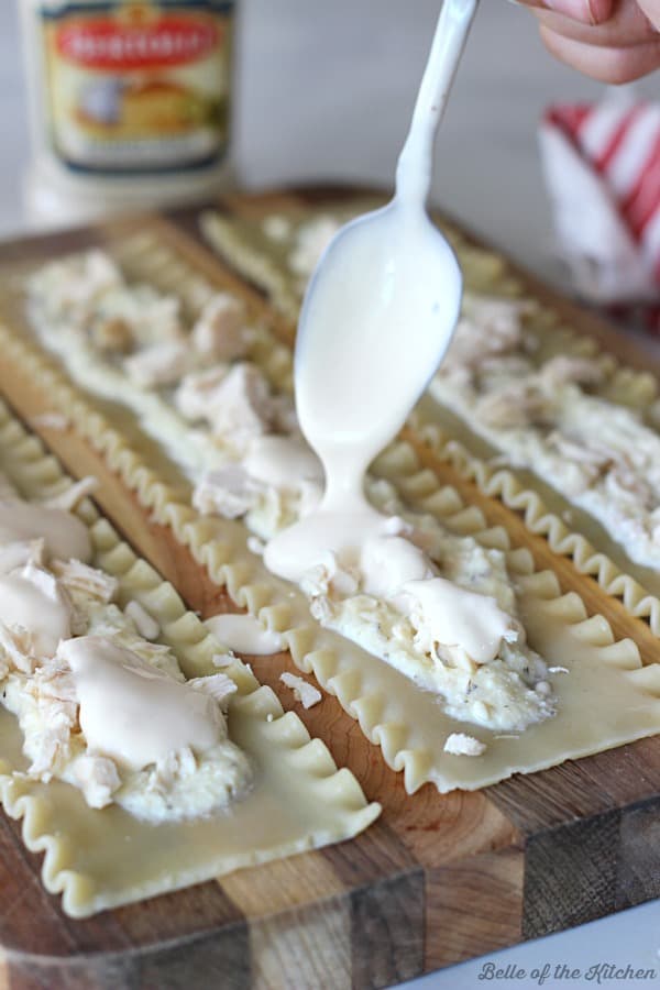 A close up of a cutting board with a lasagna noodles filled with chicken, cheeses and sauce