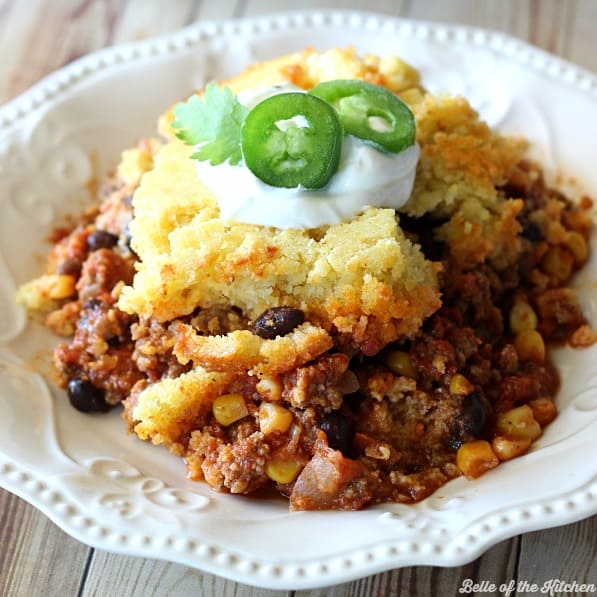 A plate of food chili with cornbread, sour cream, and slice jalapeño on top